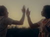 Two women standing face to face at sunset, arms raised in front of them until their hands almost touch