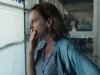 A photograph of a woman, her hand covering her mouth in a gesture of worry, stares out a window. 