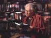 A photograph of Rudollfo Anaya reading a book in his study