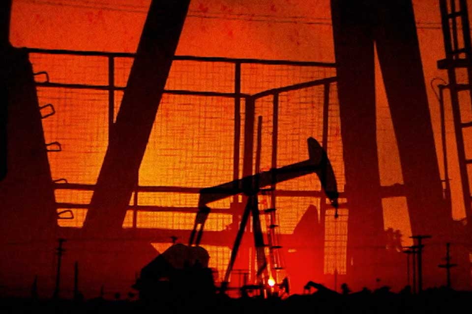 A dramatic photo of numerous oil wells pumping in a dark orange sunset