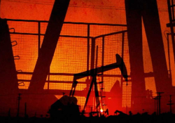 A dramatic photo of numerous oil wells pumping in a dark orange sunset