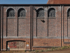 A small patch of graffiti mars the doorway of an imposing wall with tall windows up top. The wall has small text painted meticulously painted across its entire surface