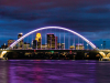 The skyline of Minnepolis seen through an arched bridge suspended over purple water