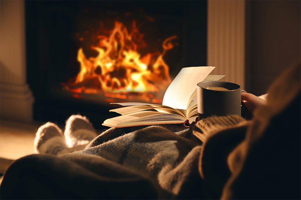 A photograph of a person sitting in front of a fire reading