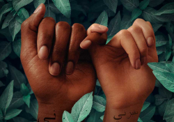 A digital illustration. Two dark skinned hands are bound by a interwoven pinky fingers. Both hands have words in Arabic written on the wrist.