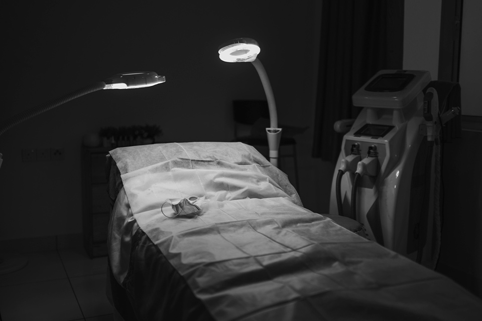 A photograph of a hospital bed bathed in light in a room swathed in shadow