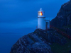 A photograph of a lighthouse perched on the face of a cliff, shrouded in blue dusk