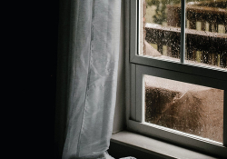 A rain laced window shot from inside a room draped in shade