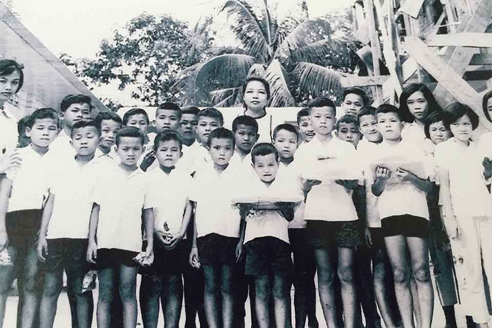 A black and white photograph of a woman standing behind a group of children