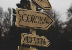 A photograph of a sign. One one arrow, text reads: Corona. On another, text reads: Lockdown.