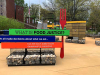 A photograph of an outdoor art installation. In the foreground, an oversized fork stands besides signs that read, "What is food justice? We all makes decisions about what we eat...but we don't make those decisions by ourselves.”