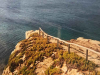 A rough dirt road terminates at the end of a point that sits on a cliff above a wine-dark sea