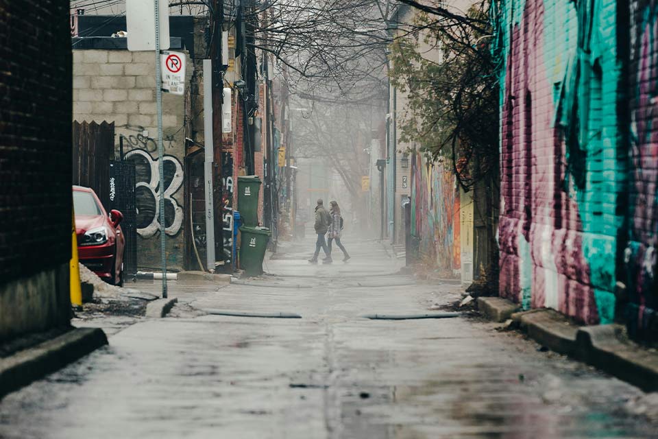 A photograph looking down a city alley. A couple holding hands strides away from the camera in the distance.