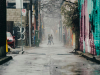 A photograph looking down a city alley. A couple holding hands strides away from the camera in the distance.