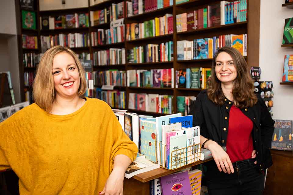 Two women smile at the camera in a bookstore