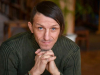 A photograph of author Volodymyr Vakulenko, his hands clasped under his chin as he looks at the camera