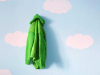 A bright green sweater hanging on a wall painted sky blue with clouds